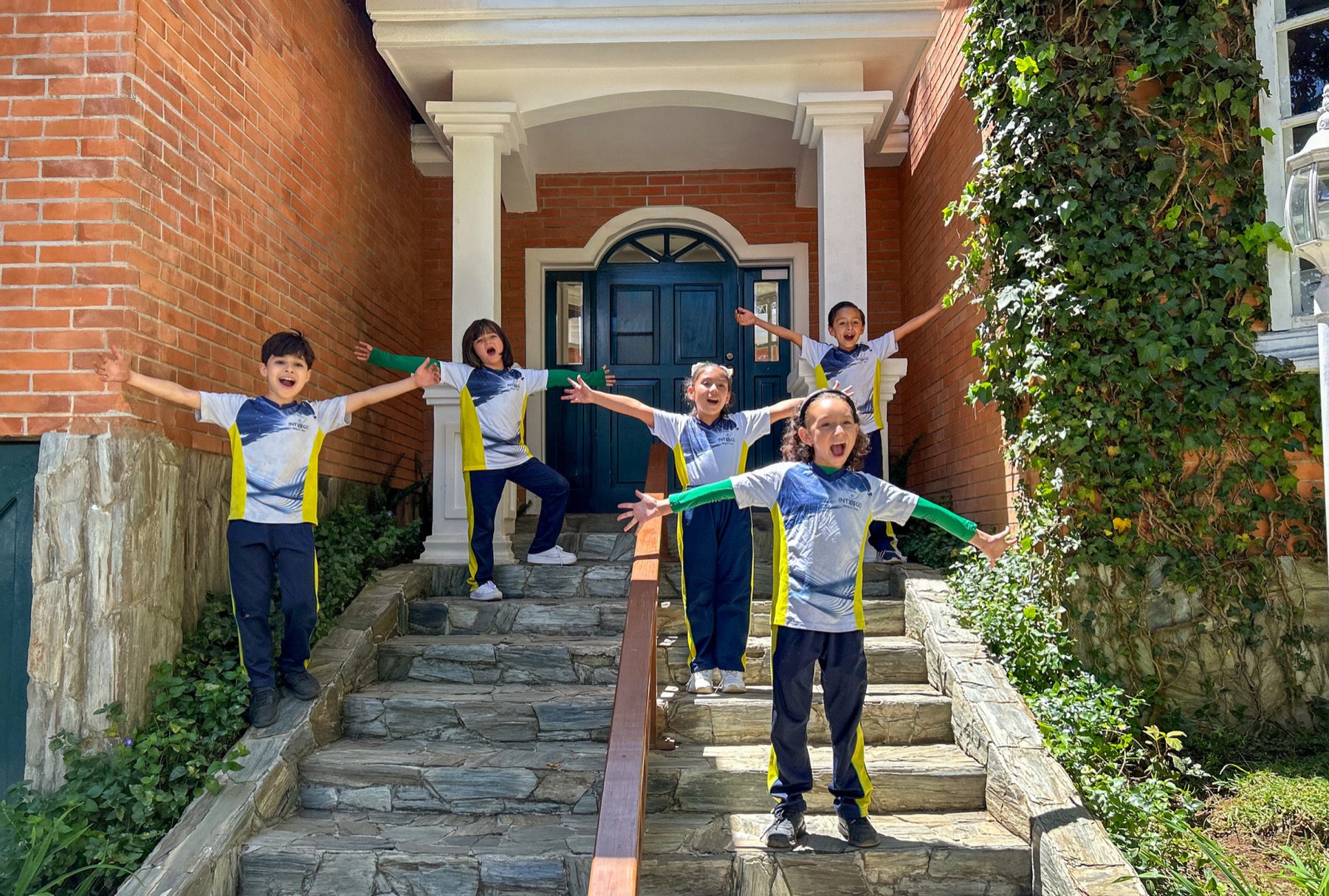 Alumnos de primaria con los brazos abiertos en las gradas de la entrada del colegio